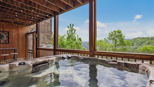 Ein Whirlpool mit einer Holzterrasse und großen Fenstern mit Blick auf eine grüne Landschaft.