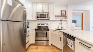 A modern kitchen with stainless steel appliances, white cabinetry, and a wooden floor.