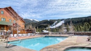 A pool area with a wooden building, lounge chairs, and a mountainous backdrop.
