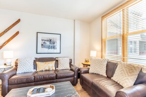 A cozy living room with a brown leather sofa, two side tables with lamps, a framed picture on the wall, and a window with blinds. - 3 Minute Walk to Gondola w/ hot tub, pool, sauna! (Keystone)