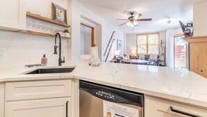 A modern kitchen with a dishwasher, a ceiling fan, and a dining area with a table and chairs.