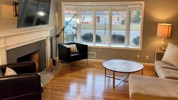 A living room with a fireplace, a flat-screen TV mounted above it, a round coffee table, and a sofa. - Southdale Stinger! Modern 5+BR near it all (Edina)