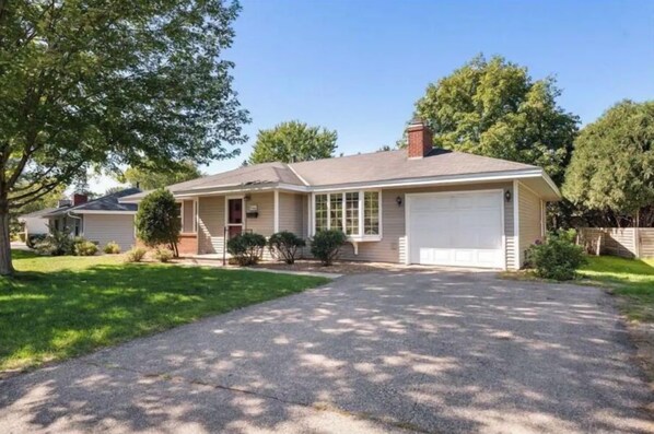 Une maison de plain-pied avec un garage, une pelouse devant et une allée.