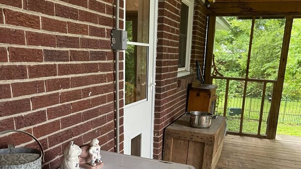 A covered outdoor area with a brick wall, a white door, and a wooden deck. - Cozy, Clean, and Convenient (Parsons)