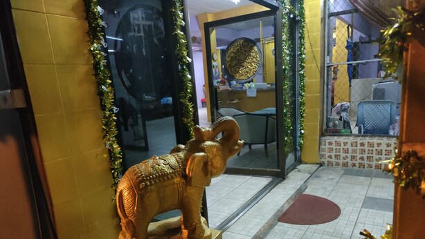 A golden elephant statue on a pedestal in a room with tiled flooring, a glass door, and a yellow wall. - Thai smile serviced Appartments (Pattaya)