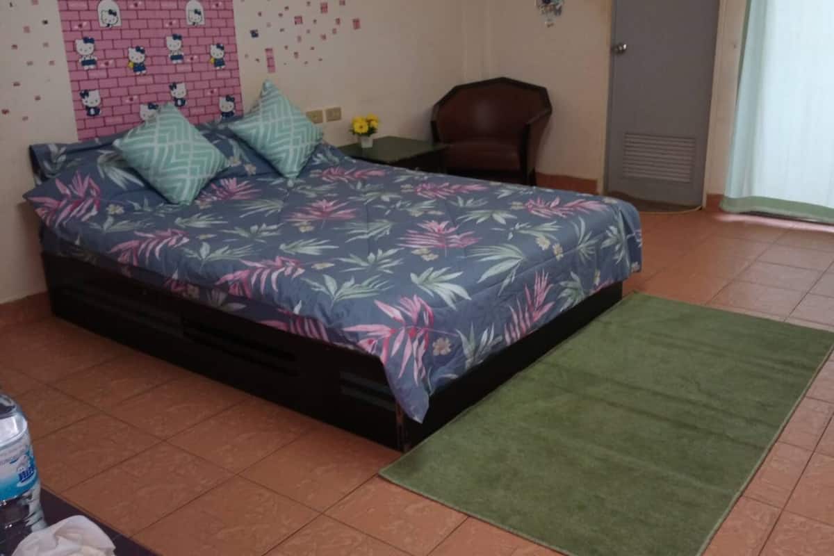 A bedroom with a floral bedspread, a green rug, a brown leather chair, and a pink wall with Hello Kitty decorations.