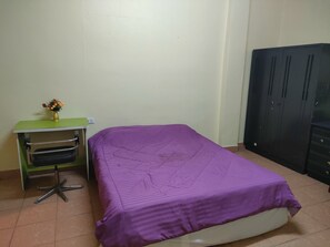 Quarto com cama, escrivaninha com cadeira, guarda-roupa e um vaso de flores.