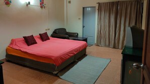 A hotel room with a bed, a desk, a chair, an air conditioner, a door, and a curtain. - Thai smile serviced Appartments (Pattaya)