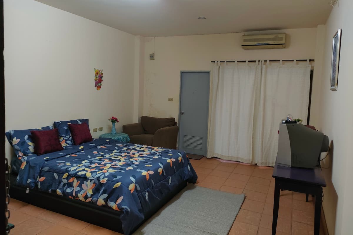 A bedroom with a bed, a chair, a desk, and an air conditioning unit.