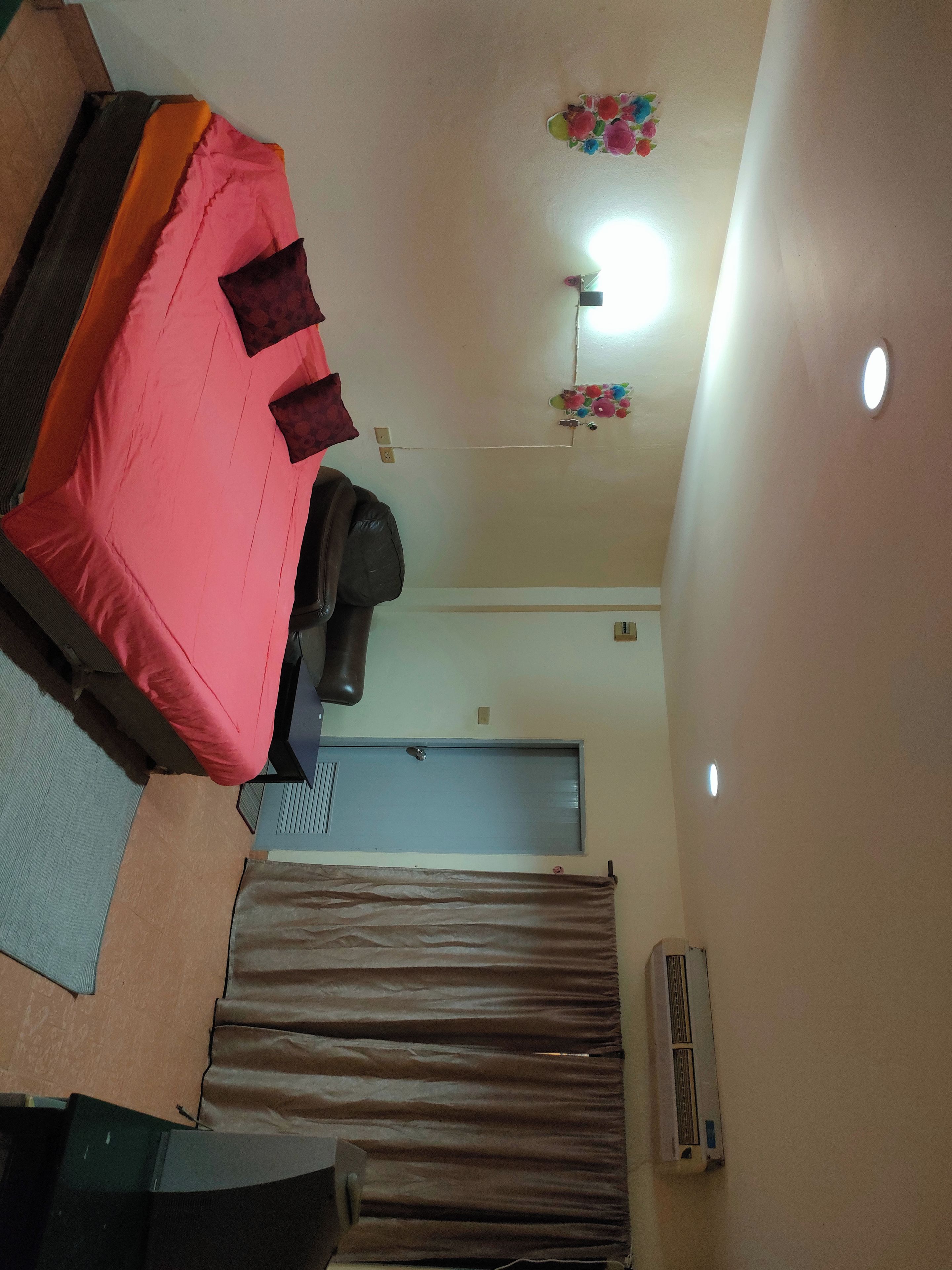 A room with a bed, a desk, a chair, a wardrobe, a door, and an air conditioning unit.
