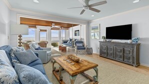 A spacious living room with a large TV, a wooden coffee table, and a ceiling fan. - Beach Club Villa 30 - Oceanfront! Pool! Walkout! (Isle of Palms)