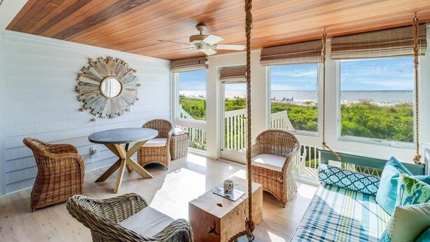 A sunlit room with a ceiling fan, wicker furniture, a round mirror, and a view of the sea. - Beach Club Villa 30 - Oceanfront! Pool! Walkout! (Isle of Palms)