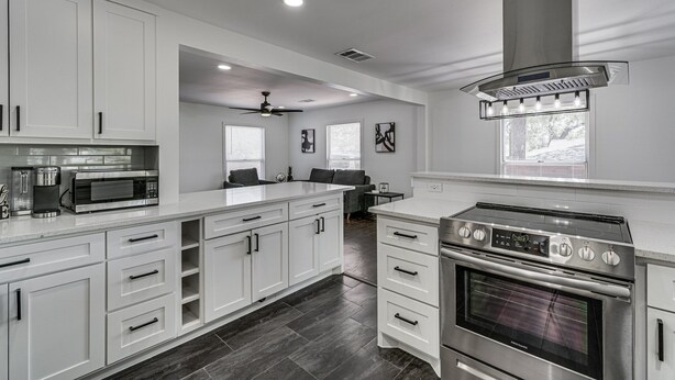 A modern kitchen with white cabinetry, a stainless steel stove, and a microwave. - Luxury Home w/ Volleyball, Golf, & Sports (Irving)