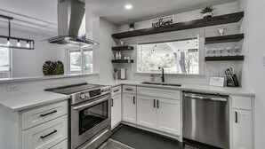 A modern kitchen with white cabinetry, stainless steel appliances, and a 'welcome' sign above the window. - Luxury Home w/ Volleyball, Golf, & Sports (Irving)