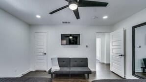 A modern room with a black sofa, a ceiling fan, and a flat-screen TV mounted on the wall. - Luxury Home w/ Volleyball, Golf, & Sports (Irving)