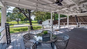 A covered outdoor area with a table and chairs, a welcome sign, and a view of a green landscape. - Luxury Home w/ Volleyball, Golf, & Sports (Irving)