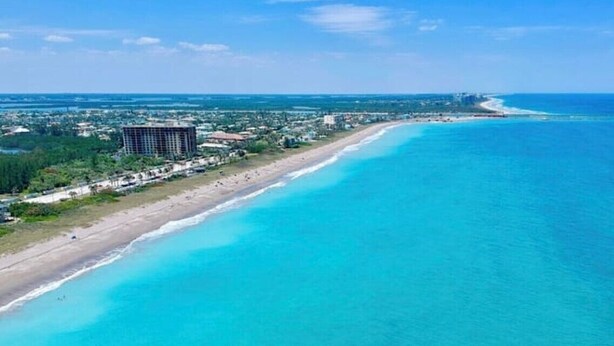 An aerial view of a coastal area with a long stretch of beach, a large building, and a clear blue ocean.