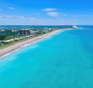 An aerial view of a coastal area with a long stretch of beach, a large building, and a clear blue ocean.