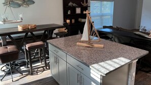 A modern kitchen with a granite island, bar stools, pendant lights, and a sailboat decoration.