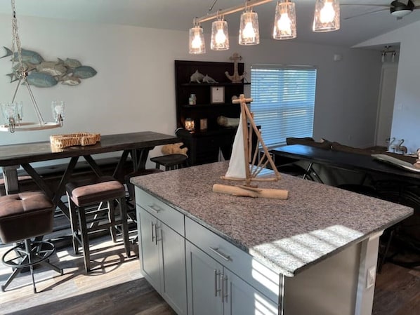 A modern kitchen with a granite island, bar stools, pendant lights, and a sailboat decoration.