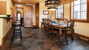 A dining area with a wooden table and chairs, a chandelier, and a view of the outside through large windows. - Outpost: Grand View 491A (Jackson)