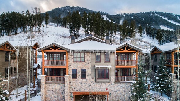 A multi-story lodge with stone walls and wooden balconies, set against a snowy mountain backdrop. - Outpost: Grand View 491A (Jackson)