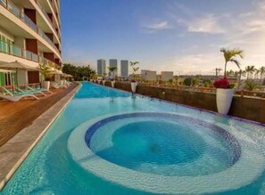 A swimming pool with a circular pattern, surrounded by a wooden deck and lounge chairs. - CONDO D12 BY TRVL2HM (Puerto Vallarta)