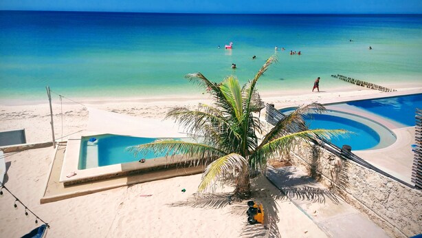 Une plage avec une piscine, des palmiers et un ciel bleu azur.