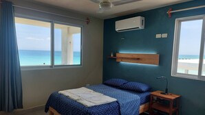 Une chambre avec un lit, une table de chevet, un ventilateur de plafond, un appareil de climatisation et une vue sur l’océan.