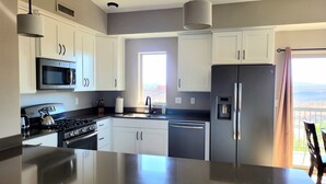 A modern kitchen with stainless steel appliances, white cabinets, and a large island. - Beautiful New 2 Bedroom Condo in the heart of St. George (St. George)