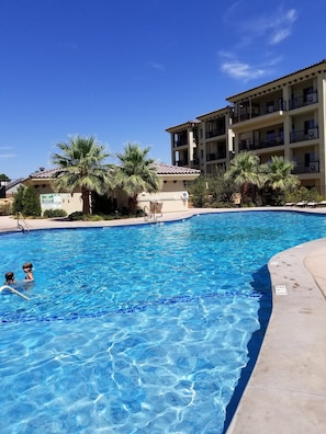 Une piscine à l’eau d’un bleu cristallin, entourée de palmiers et bordée d’un immeuble à plusieurs étages doté de balcons.