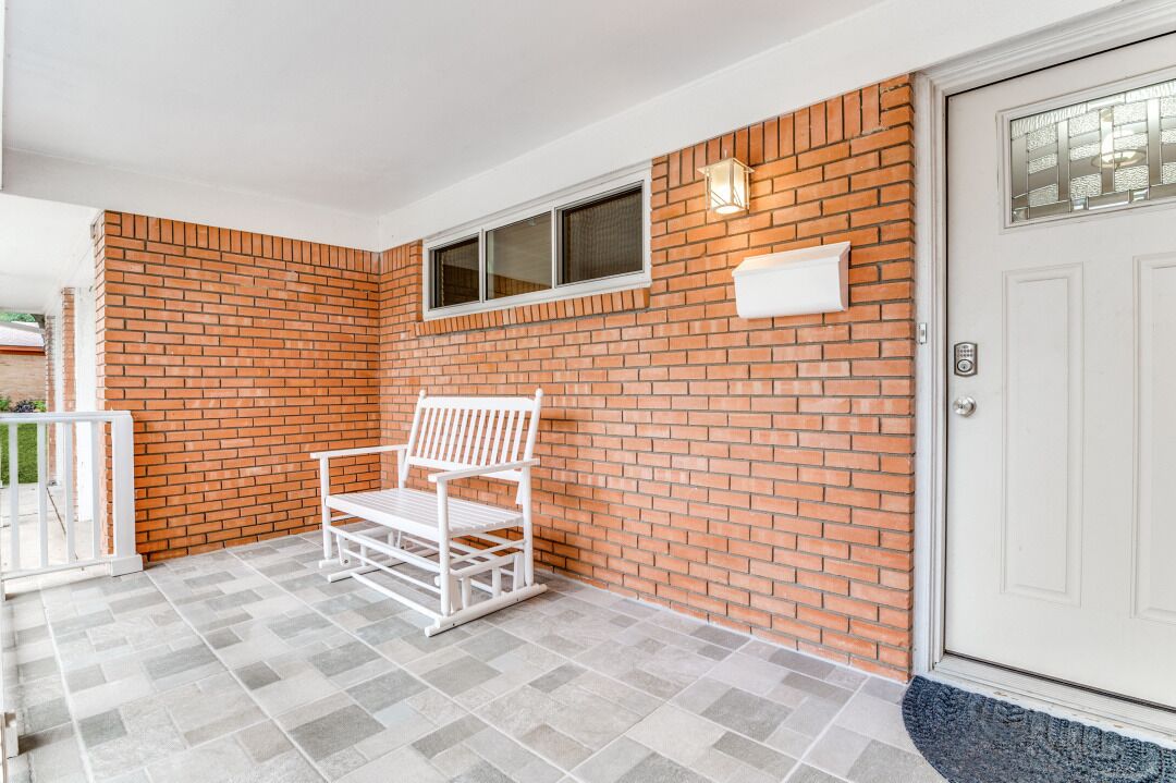Een overdekte veranda met een witte bank, een bakstenen muur en een witte deur.