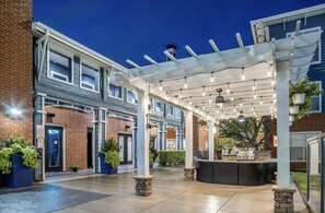 A covered outdoor patio area with a pergola, seating, and potted plants.