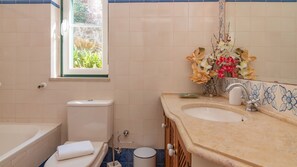 Un baño con inodoro, lavabo y bañera. Se ve un ventanal con vistas a la vegetación.