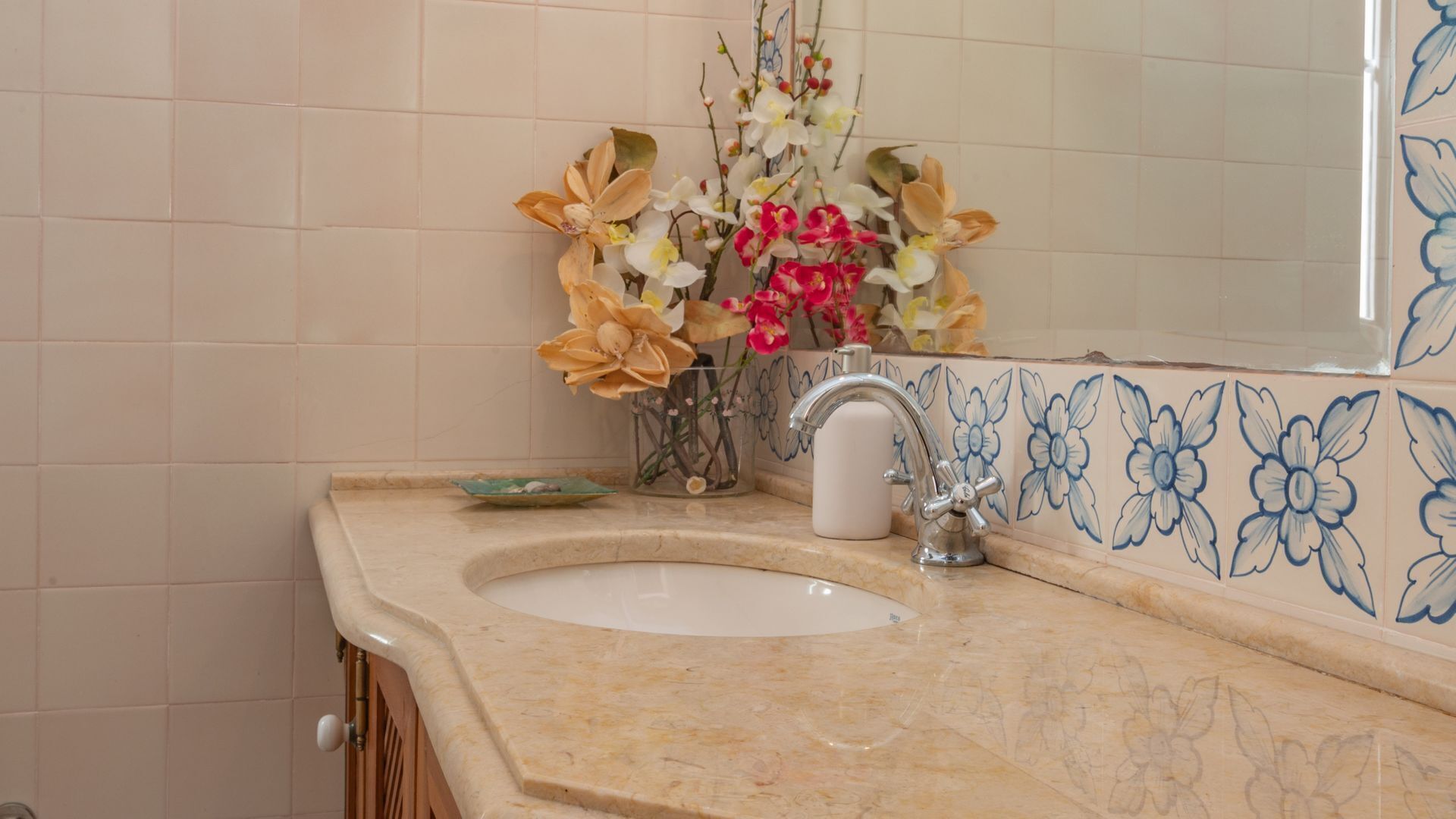 Une salle de bain avec un lavabo en marbre, un miroir et un mur recouvert de carreaux à motifs floraux.