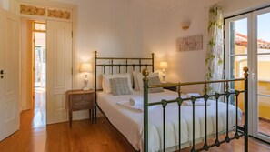 Un dormitorio con cama con dosel, dos mesitas de noche con lámparas, una mesita de madera y vistas a través de un ventanal.