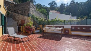Un patio con una tumbona, una mesa con mantel, plantas en macetas y una pared de piedra.