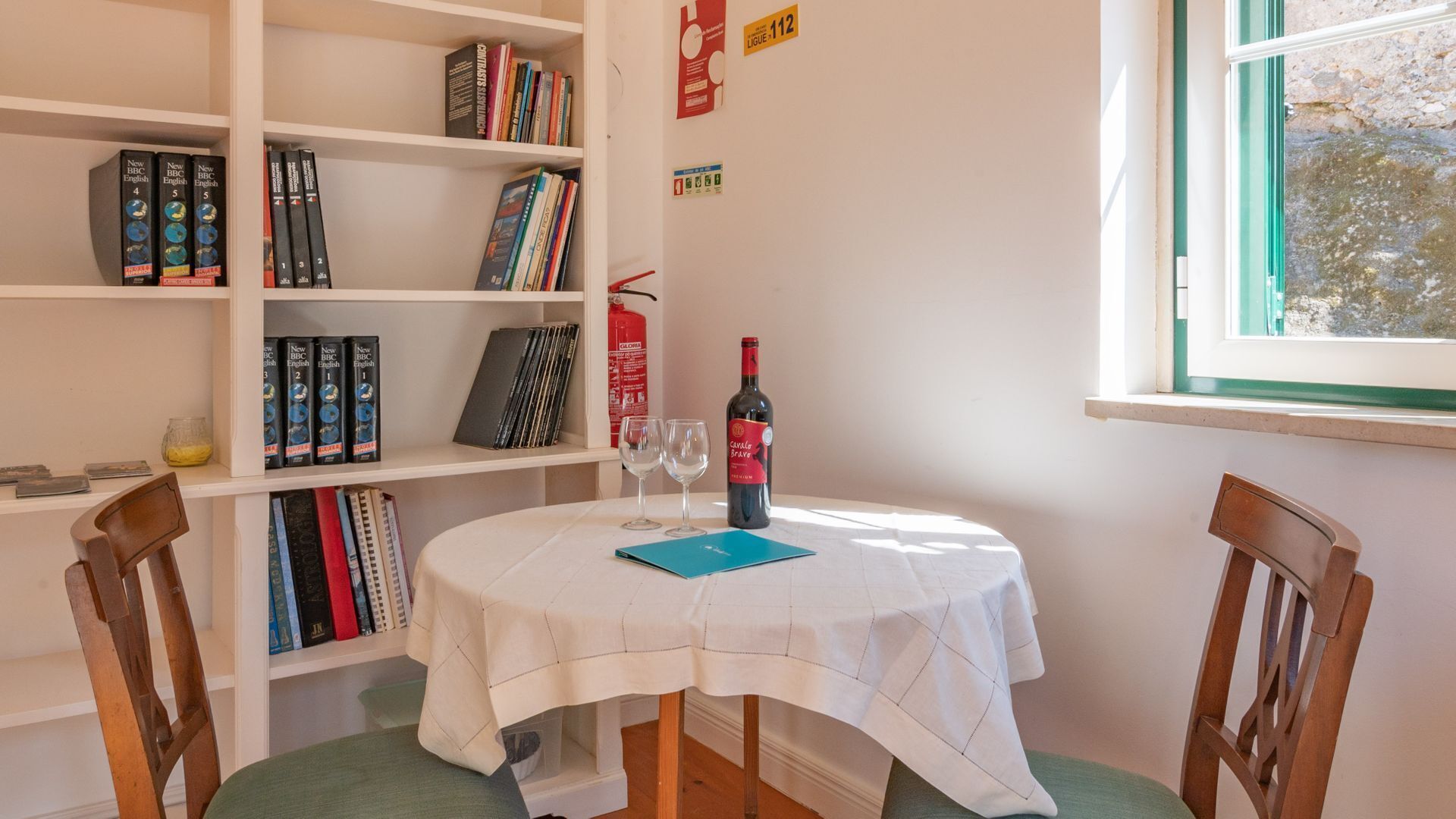 Ein Zimmer mit einem runden Tisch, zwei Stühlen, einem Bücherregal und einem Fenster.