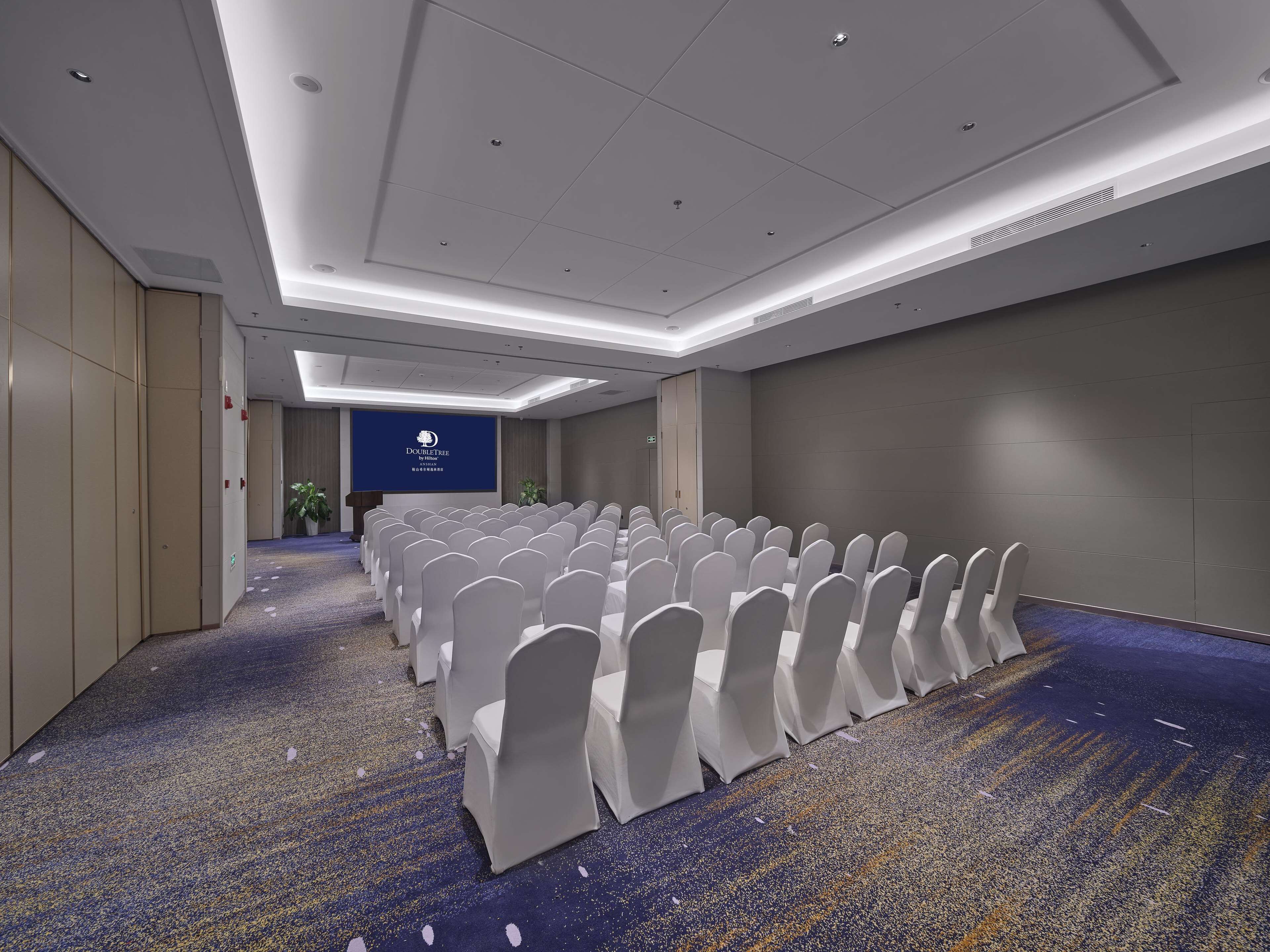 A conference room with rows of white chairs, a podium, and a screen displaying the DoubleTree logo.