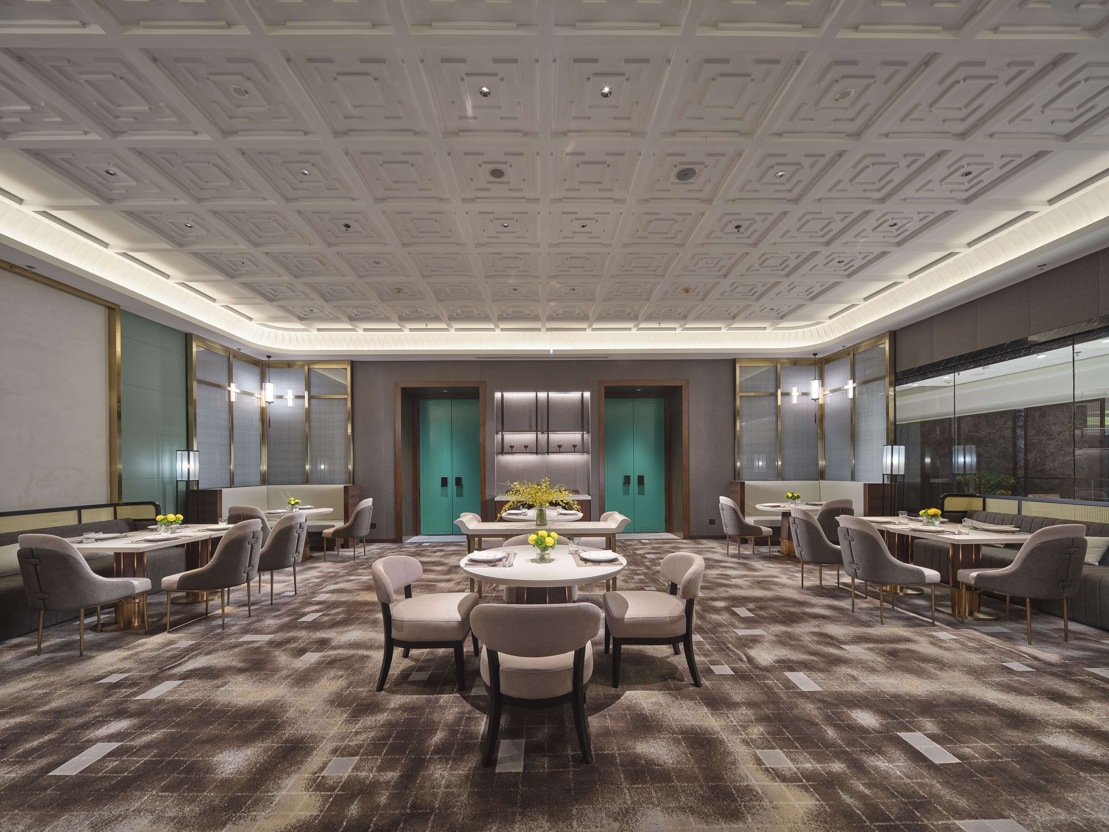 Un salón de conferencias moderno en un hotel con diseño geométrico en el techo, mesas redondas y asientos cómodos.