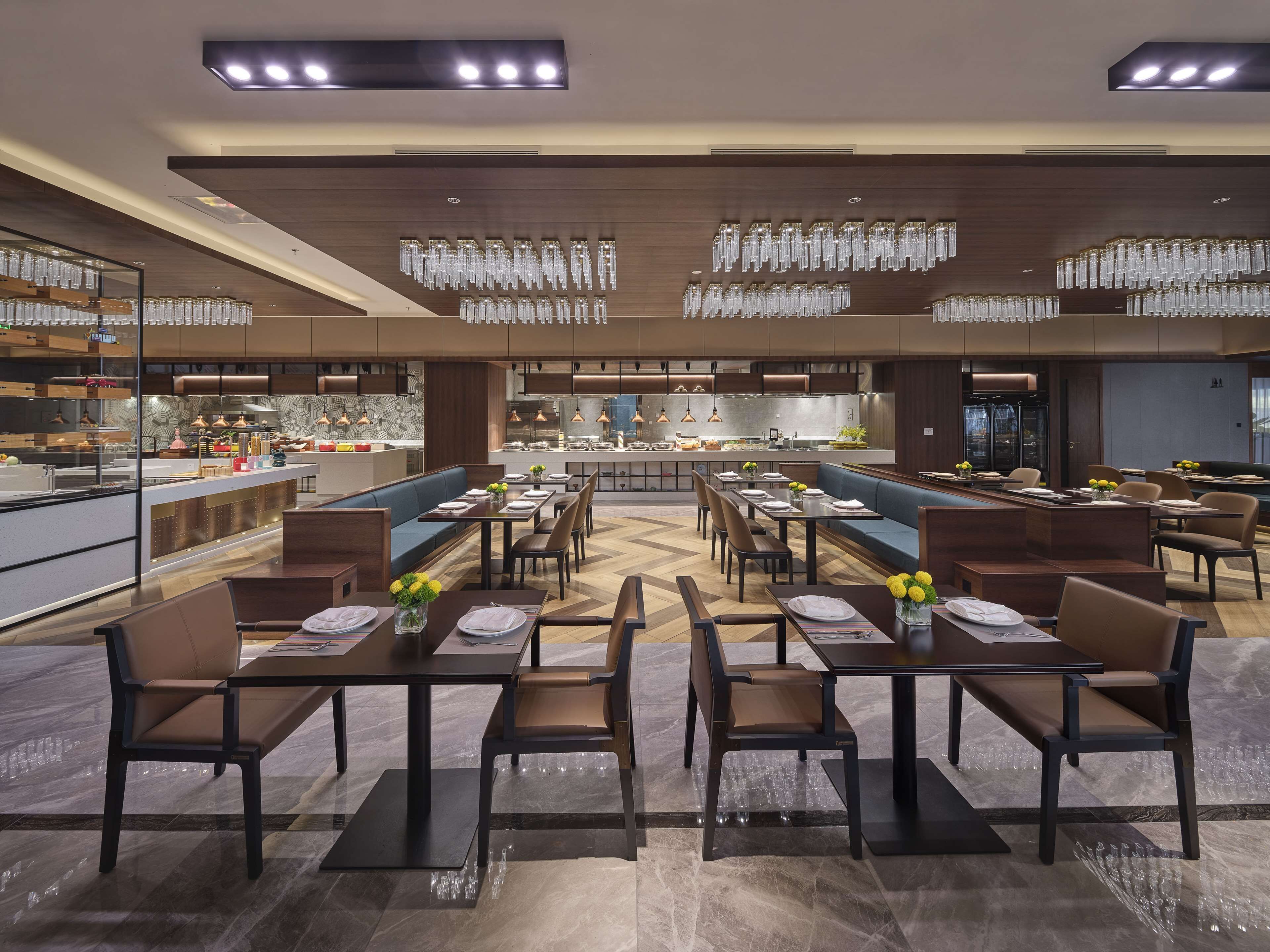 A modern restaurant with a central bar, multiple dining tables, and a kitchen area.