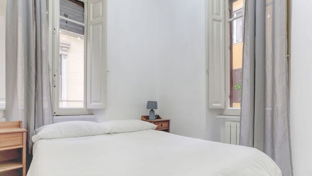 A bedroom with a bed, a nightstand with a lamp, and a window with curtains. - Charming Colosseum - HOME AND MORE (Roma)