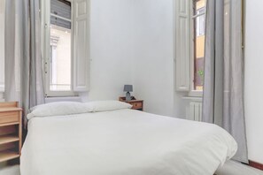 Quarto com uma cama, mesa de cabeceira com abajur e janela com cortinas.