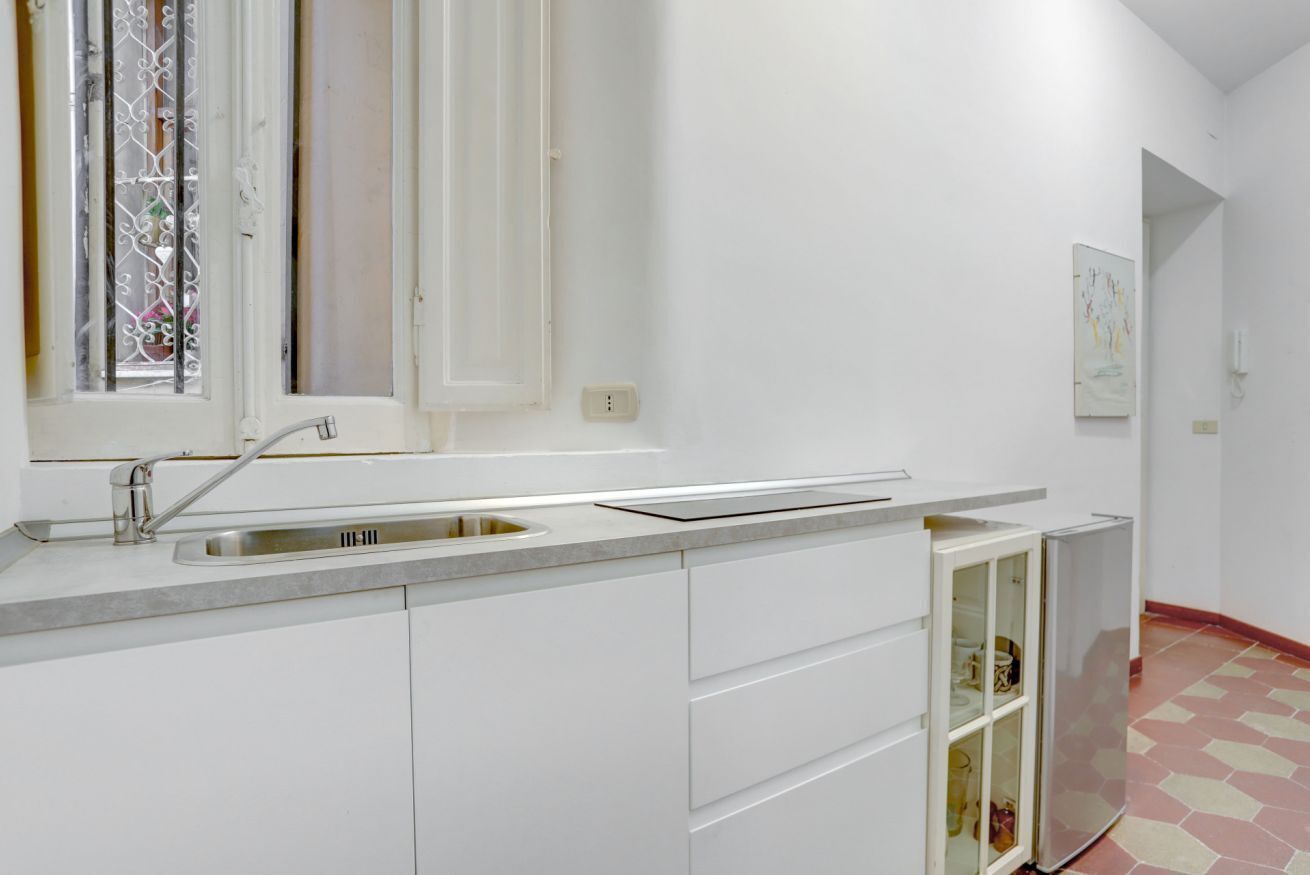 Una cocina con pileta de acero inoxidable, alacenas blancas y un mueble con puerta de vidrio.