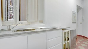A kitchen with a stainless steel sink, white cabinets, and a glass-fronted cabinet. - Charming Colosseum - HOME AND MORE (Roma)