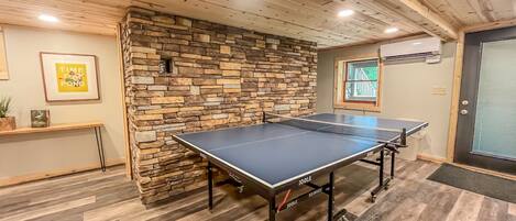 Una mesa de ping pong en una habitación con suelo de madera, pared de piedra y una puerta con ventana.