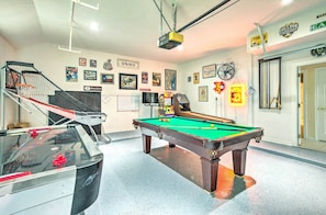 Una mesa de billar en una habitación con una escalera, un proyector y diferentes adornos en las paredes.