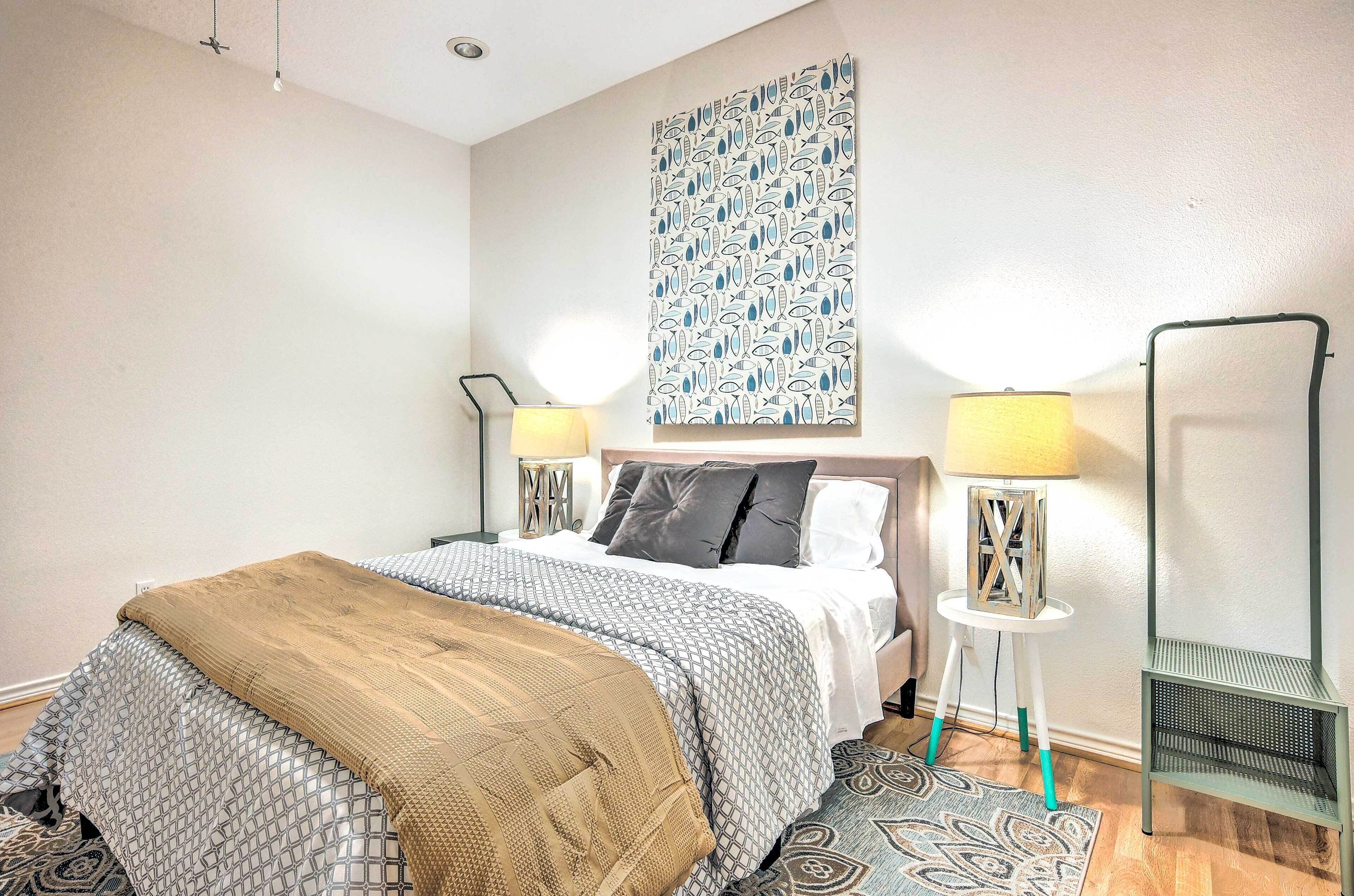 A neatly arranged bedroom with a bed, two bedside tables with lamps, a green chair, and a patterned wall hanging.