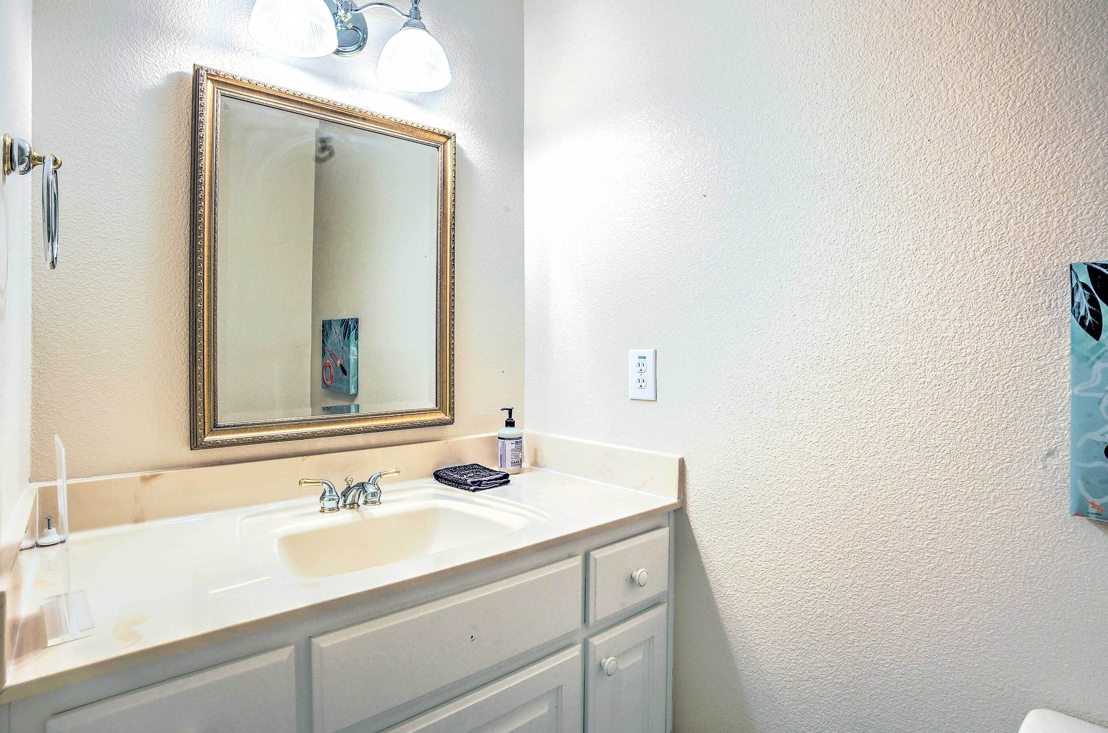 A bathroom with a white sink, a large mirror with a gold frame, and a wall-mounted light fixture.