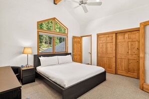 A bedroom with a bed, a nightstand, a lamp, a window with a view of trees, and wooden doors.